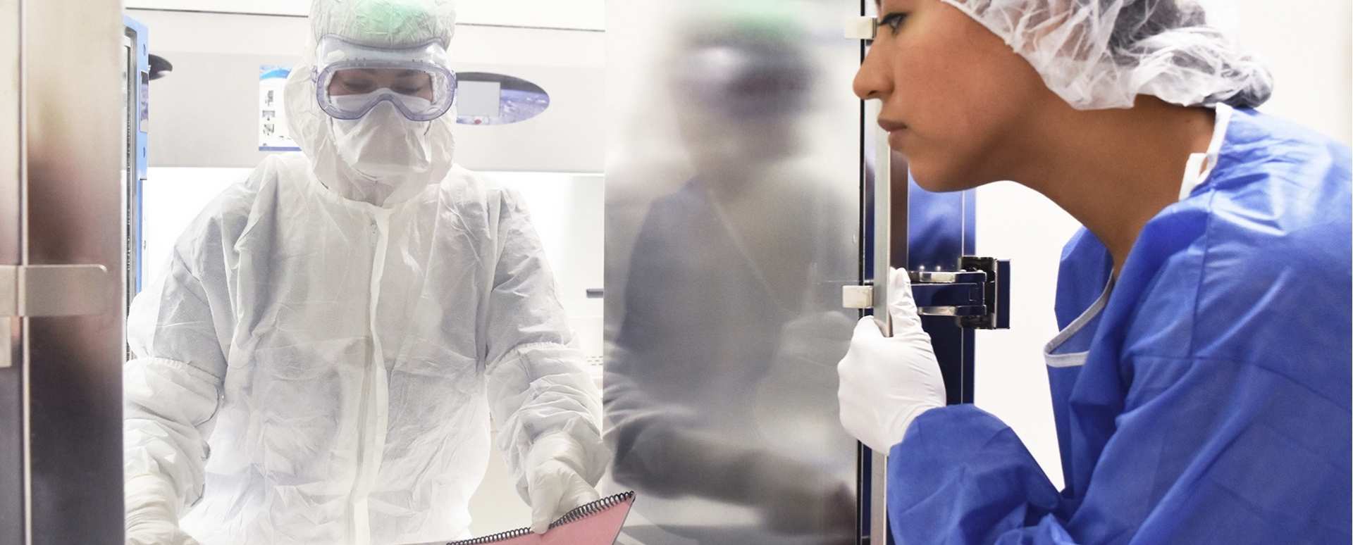 Une personne en combinaison blanche, avec des gants blancs et des lunettes de sécurité de laboratoire, remet un rapport relié avec une couverture rouge à travers une fenêtre avec une porte à une femme avec des gants blancs, une combinaison bleue et un filet à cheveux.