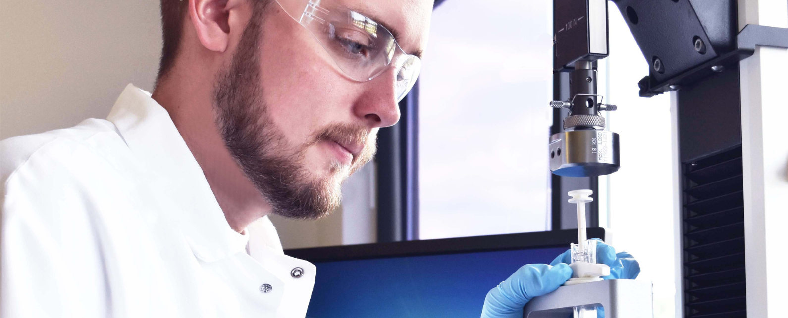 Un homme en blouse et lunettes de laboratoire utilise une machine Instron pour tester une seringue.