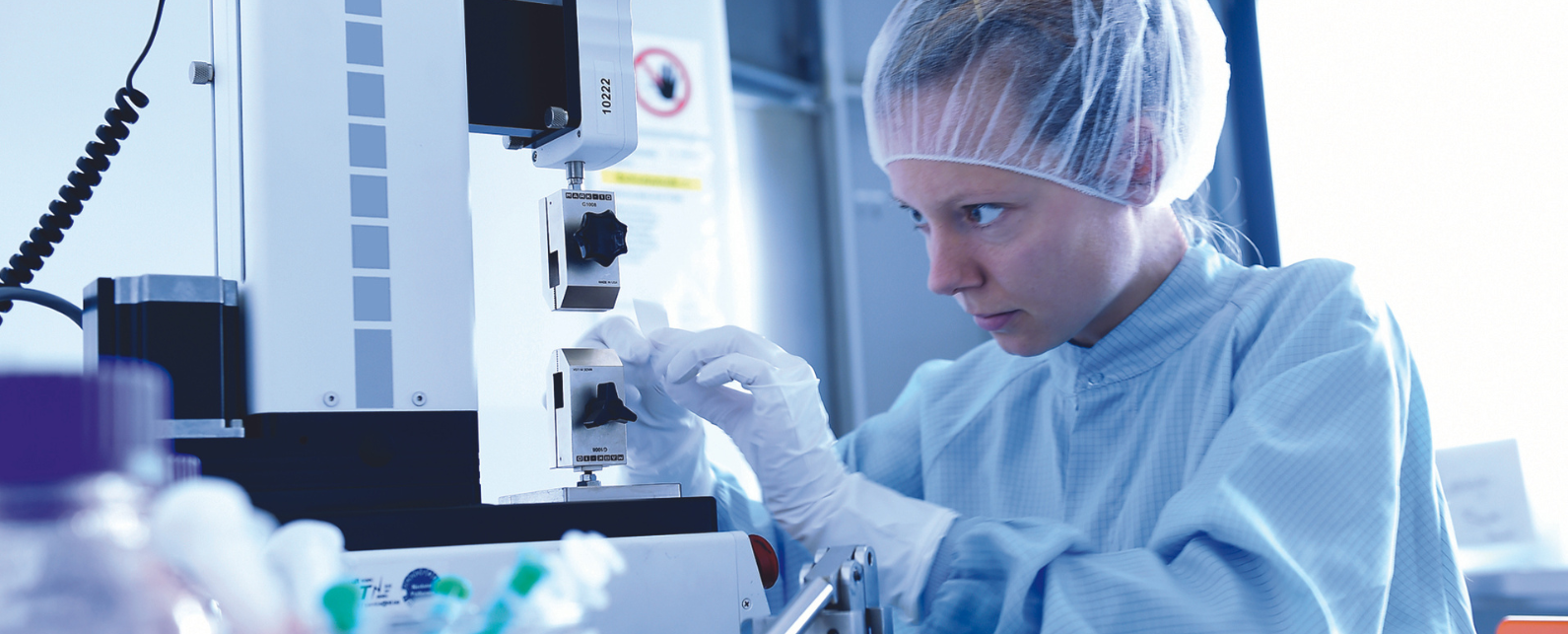 femme en blouse de laboratoire, gants et bonnet de cheveux, utilisant une machine